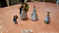 Four Royal Doulton and Avon porcelain figurines placed on a table covered with a pink tablecloth, showing scale and overall condition.