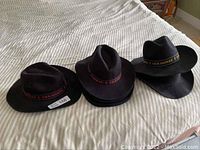 Three black felt cowboy hats with Seahorse branded hat bands in red and yellow, placed on a bed.