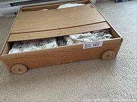 Wooden wheeled under bed sliding drawer partially opened revealing floral sheets.