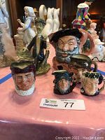 Front view of five Royal Doulton Toby mugs displaying various character faces and sizes on a pink tablecloth.