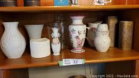 Shelf with eight assorted vases including white ceramic, porcelain with floral decorations, and clear glass.