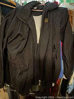 Black jacket on hanger, polyester or similar fabric, front zipper, longer fit style