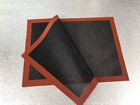 Photo showing two silicone baking mats with black perforated centers and red borders, one mat folded to display flexibility and texture.
