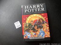 Front cover of first edition Harry Potter and the Deathly Hallows hardcover book showing title, author and colorful illustrated cover art.