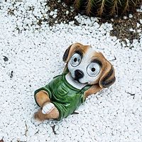 Photo showing the detailed relaxed dog figurine lying on white decorative stones, highlighting green overalls and painted fur patterns.