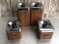 Photo showing full set of four vintage kitchen canisters with faux wood sides and chrome lids labeled sugar, flour, coffee, and tea.
