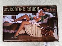 Full view of the metal tin sign showing the illustration of a reclining pin-up woman and the text 'The Casting Couch Playbook'.