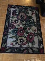 Floral patterned area rug on wooden floor, black border with multicolor flowers