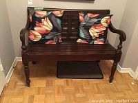 Front view of dark wood bench against wall with two floral cushions on seat