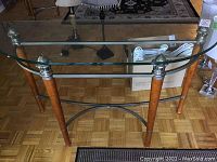 Photo of demi lune console table with glass top and wooden legs with metal accents, shown from front angle