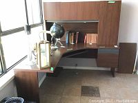 Full view of faux wood corner desk three sections with books and decorative globe on surface. Shows shape, finish and included storage compartments.