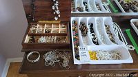 Wooden jewelry box with compartments open, plastic trays with necklaces and bracelets on table