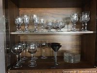 Shelf holding various crystal and glassware including wine glasses and dessert plates.