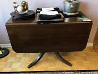 Front view of wooden drop leaf table with decorative claw feet base, leaves down, with items on top.