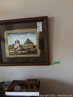 Framed Egyptian-themed artwork, depicting the Great Sphinx and a pyramid, printed or painted on fabric material with frayed edges, signed by artist.