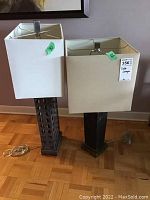 Full view of two table lamps showing metal bases and fabric square shades, arranged side by side on the floor.