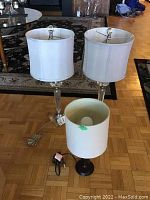 Three lamps on floor, two taller matching acrylic and metal base lamps with white shades, and one smaller wooden base lamp with white shade
