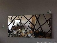 Large rectangular mirror on wall with diamond-pattern wood inlay creating multiple smaller mirror panels; reflective surface shows furnishings in room.