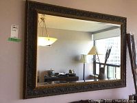 Front view of large rectangular wall mirror with ornate dark wood frame with gold highlights, hanging on wall.