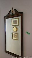 Full view of large vintage wood-framed mirror with decorative curved top and two framed art prints and small octagonal mirror reflected inside.