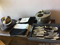 Photo showing cloth napkins, chargers, cutlery set tray, and metal wine cooler stand grouped on a surface.