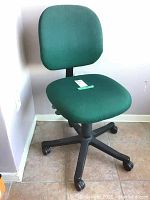 Front right angled view of the green upholstered office chair showing seat, backrest, and wheel base.