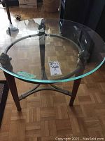 Side view of round glass-top table showing metal supports and wood legs on parquet flooring with contents not included.