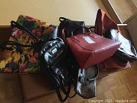 Group of assorted purses including leather-like and fabric floral tote bag, shown from side angle on table.