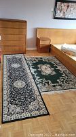 Photo showing both rugs side by side in bedroom: dark blue hallway runner and green area rug with floral designs.