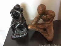 Pair of two metal statues, one dark metal with two embracing abstract human figures, the other a rustic brown abstract sitting figure