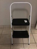 Front view of the two-step metal stool showing white metal frame and two black platforms with wear marks