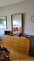 Full front view of teak dresser with matching mirror leaning against wall.
