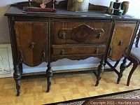 Front view of the antique wooden cabinet showing two side doors, two central drawers with decorative handles, turned legs, and wood grain detail.