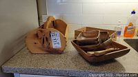 Photo showing set of wooden kitchenware including a catch-all basket, a wooden tray with four smaller serving bowls and two utensils on a countertop