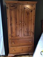 Front view of wooden armoire with closed double doors and two drawers below.