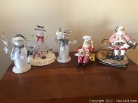 Front view of all five Christmas figurines arranged on surface including three snowmen and two Santa Claus figures.