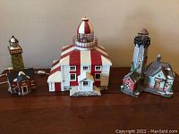 Three lighthouse figurines shown on a white background: one large white and red striped lighthouse, one medium grey lighthouse with small house, one small green lighthouse with buildings