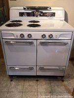 Front view of the white vintage Moffat electric stove with four coil burners and double oven doors with chrome handles.