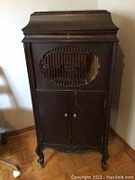 Full frontal view of dark wooden vintage record player cabinet showing front damage and ornate legs.