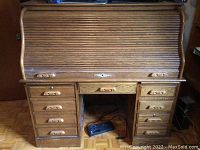 Front view of closed roll top desk with multiple drawers on both sides and center drawer.