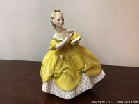 Front view of Royal Doulton figurine in yellow dress holding a white bird.