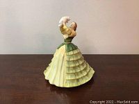 Front view of Royal Doulton figurine depicting a lady named Emily holding a white cat above her head, wearing a ruffled green and yellow dress.