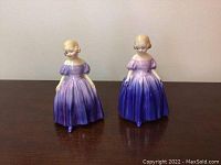Front view of two Royal Doulton Marie HN 1370 figurines showing girls in gradient purple dresses with blonde hair.