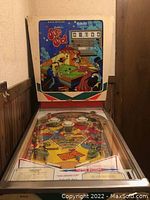 Frontal view of full pinball machine in basement hallway showing cabinet, backbox and playfield under glass