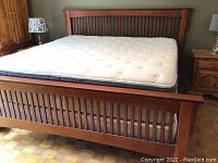 Full view of king size wood bed frame with mattress laid in place, headboard and footboard visible