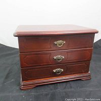 Closed view of the wooden jewelry box showing its three drawers and metal handles.