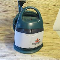 Front view of Bissell Little Green deep cleaner showing unit body, handle, hose wrapped around back, and power cord.