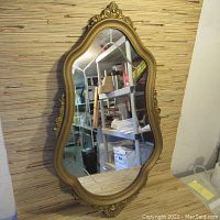 Full view of vintage decorative wall mirror showing ornate gold frame and beveled glass reflecting room interior.