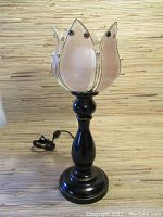 Full view of the lamp on a striped wood surface showing black base and flower shaped pink glass petal shade.