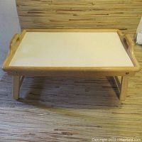 Front view of the vintage folding lap table showing white top surface, wood frame with handles, and extended legs